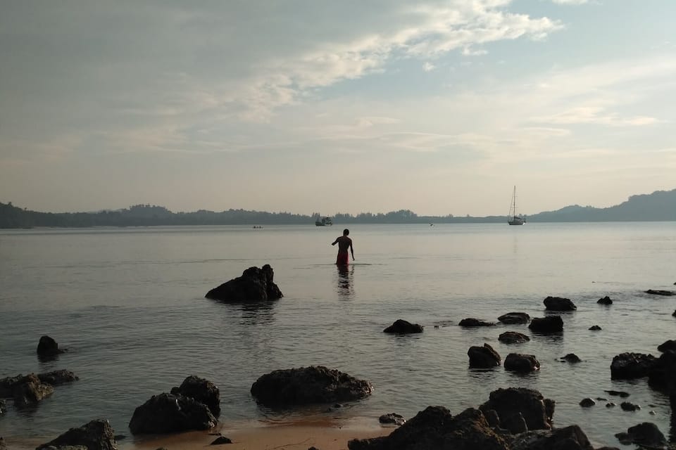 A beach with large rocks in the foreground and a person wading in the water.