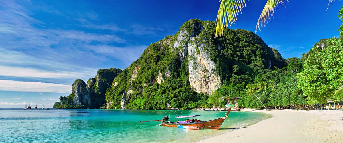 A beach with boats, a large mountain, and a clear blue sky.