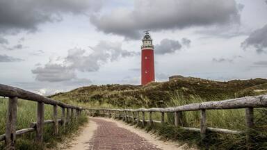 A red lighthouse on a grassy hill with a brick pathway leading to it.