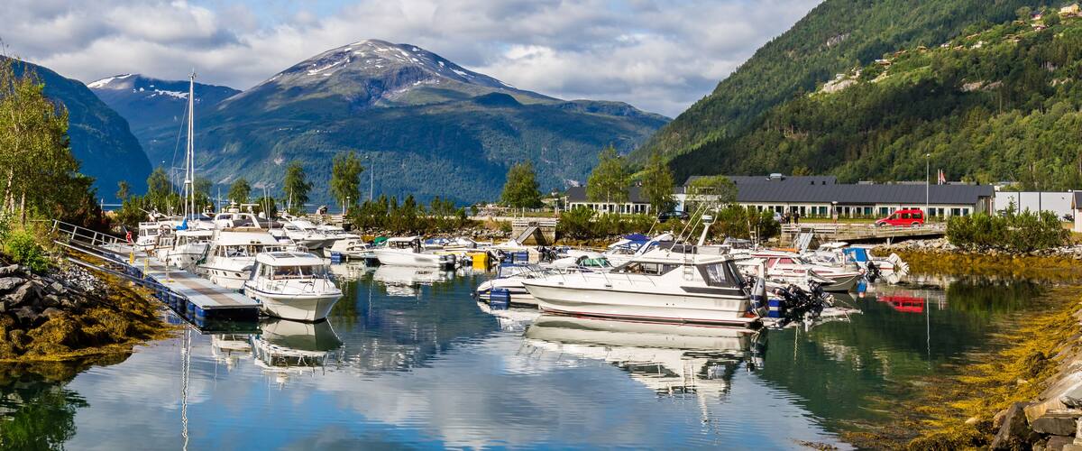 A marina with boats docked, surrounded by mountains and a small island with rocks and trees.