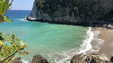 A coastal landscape with a clear turquoise sea, rocky cliffs, and a sandy beach.
