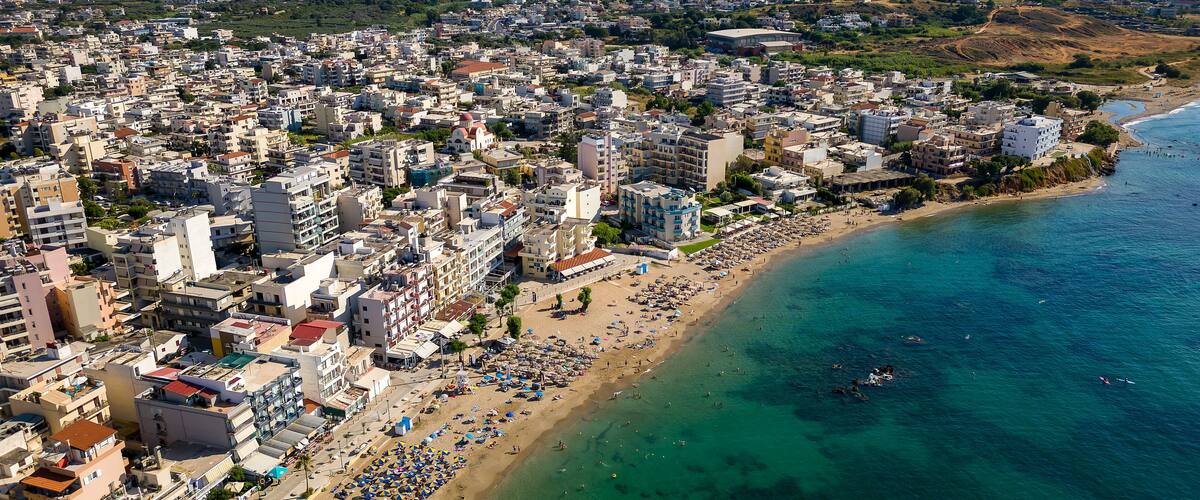 A coastal city with a densely packed urban area, a long sandy beach, and a clear blue sea.