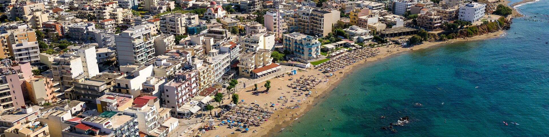 A coastal city with a densely packed urban area, a long sandy beach, and a clear blue sea.