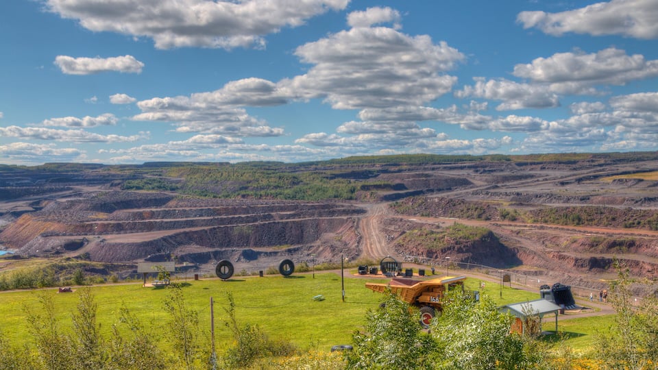 A mining landscape with open pits, large machinery, and a green field in the foreground.