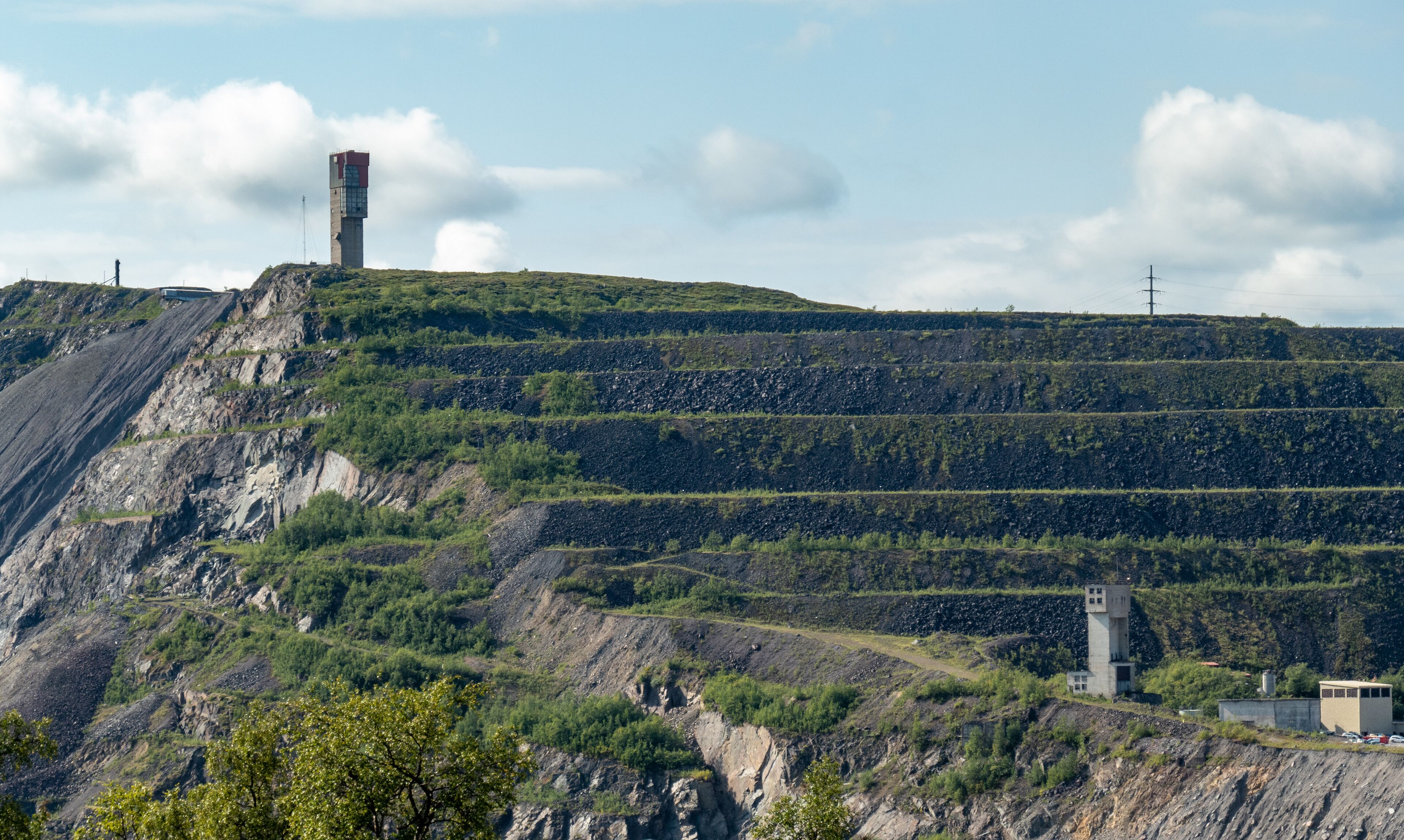 A mountainous landscape with terraced fields, a tall tower, and a smaller building.