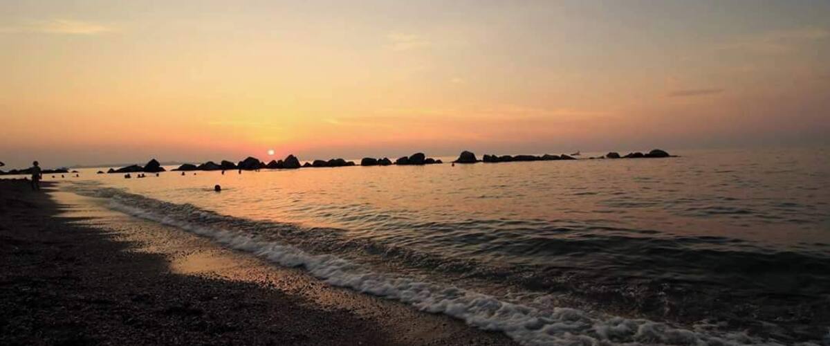 A beach at sunset with waves gently lapping the shore and distant rock formations.