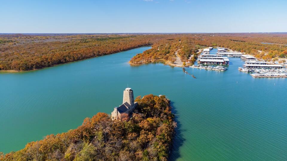 A river with a historic tower, a marina, and surrounding forested landscape.
