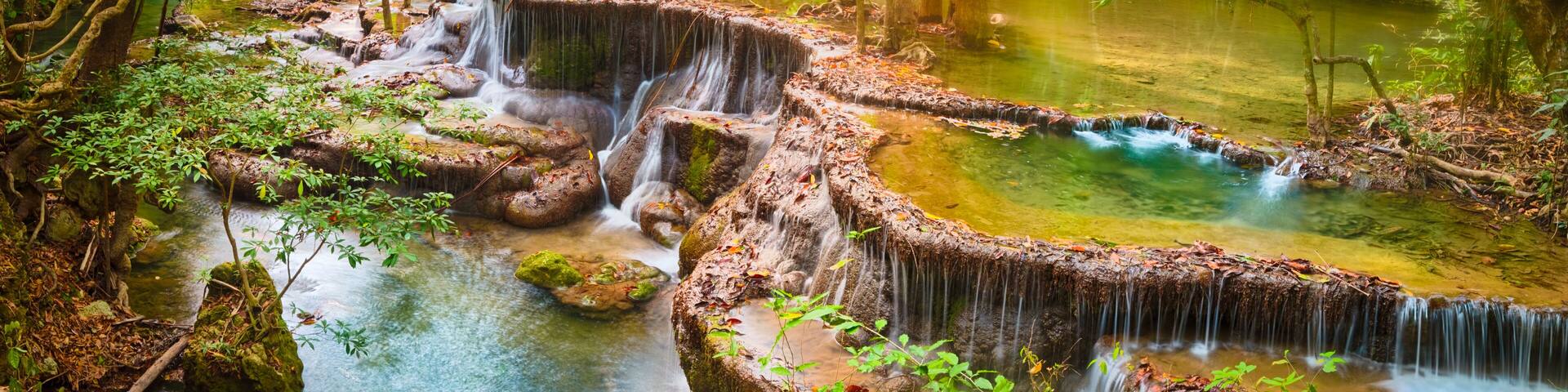 A natural waterfall in a forested area with clear water and surrounding greenery.