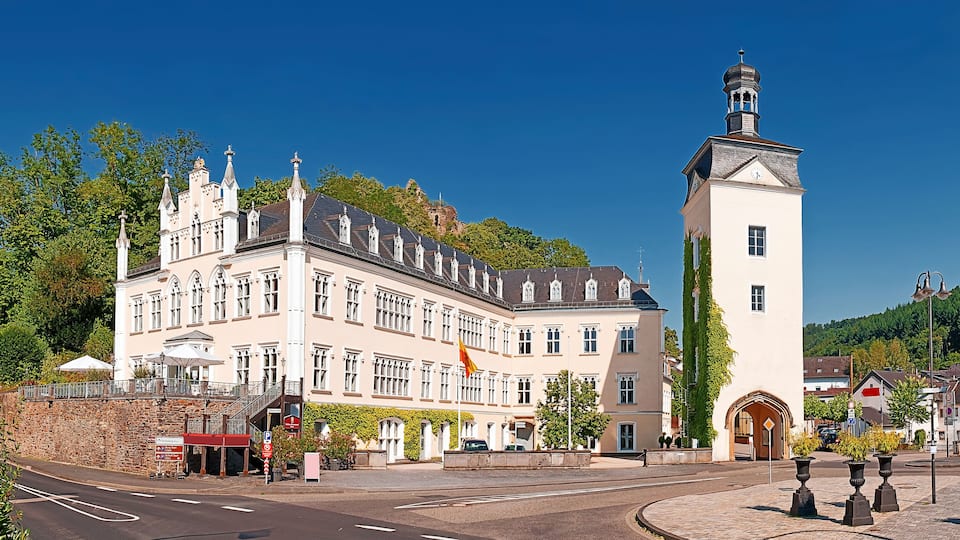 A historic building with a clock tower, surrounded by lush greenery and a clear blue sky.