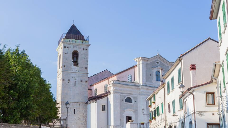 A historic tower with a bell, surrounded by traditional European buildings with green shutters.