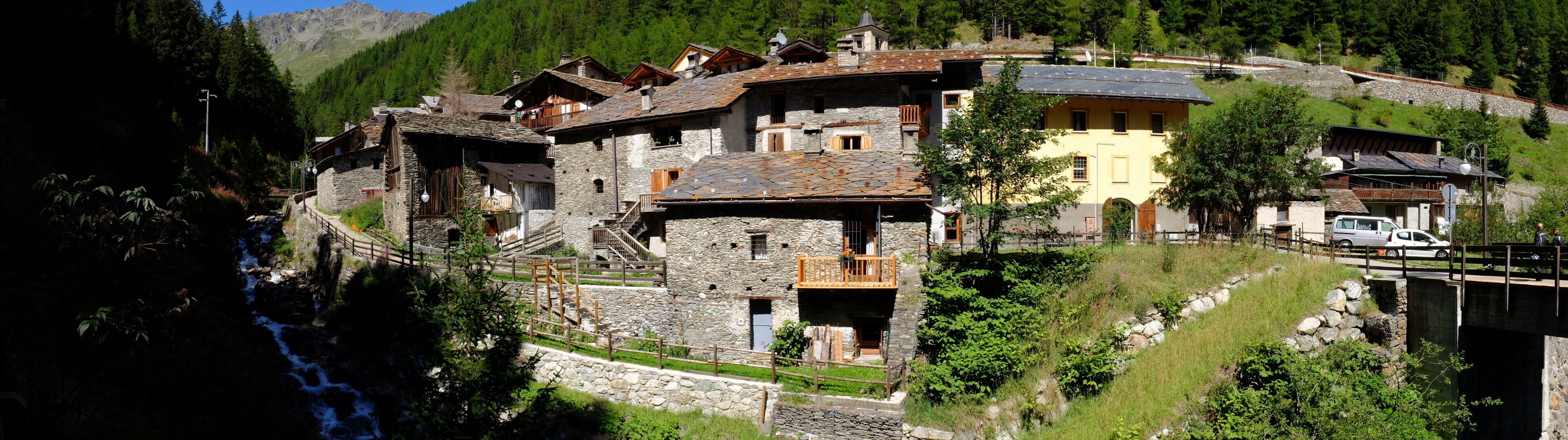 A mountain village with stone buildings, a bridge, and a flowing stream.
