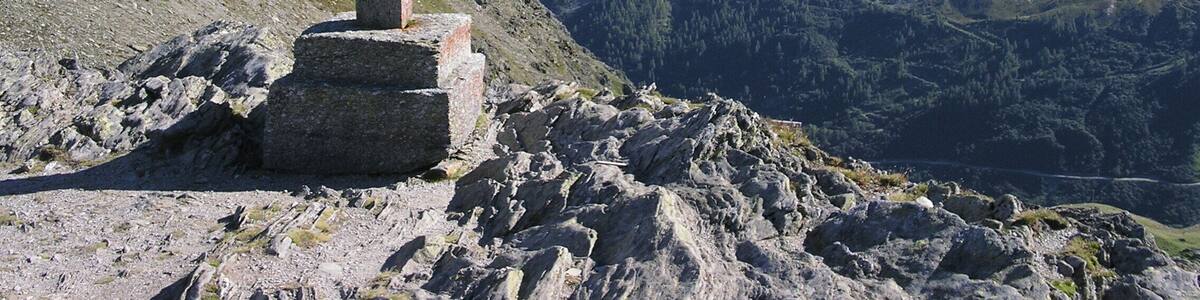 A stone cross on a mountain ridge with a valley and distant mountains in the background.