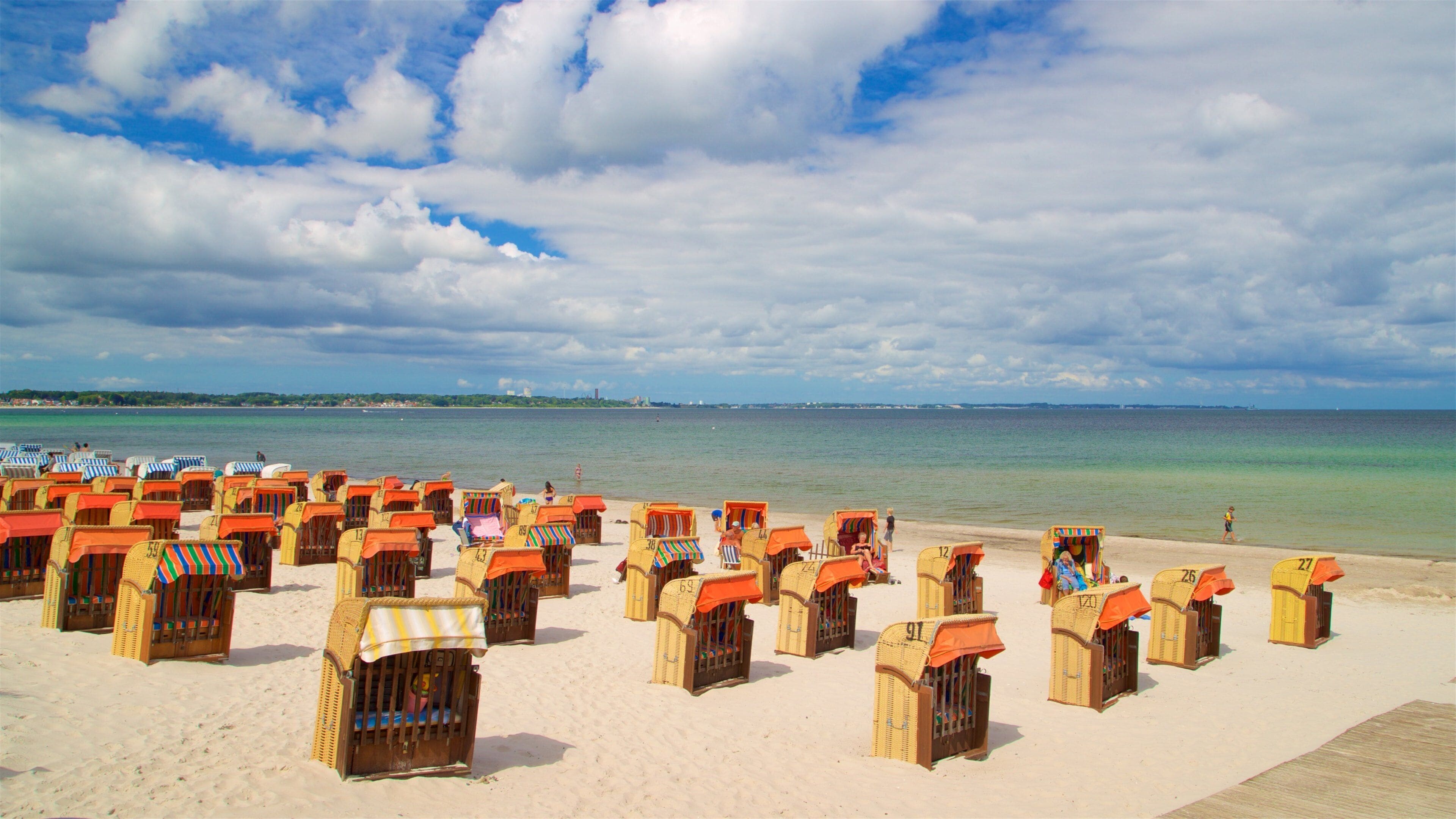 A beach with numerous wicker beach chairs with orange canopies, a clear sky, and calm sea.