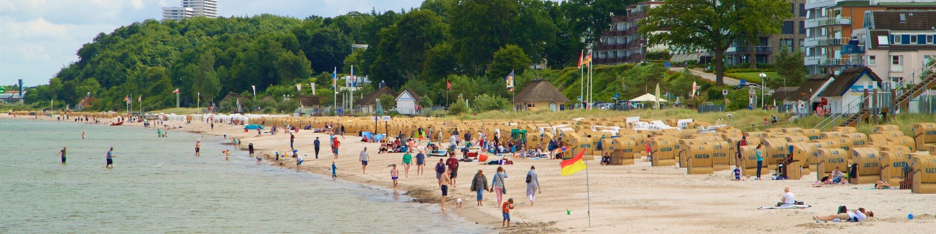 Una playa concurrida, gente, arena y una colina boscosa al fondo.