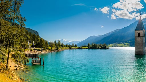 Une tour se dresse au milieu d’un lac, entourée de montagnes et d’arbres.