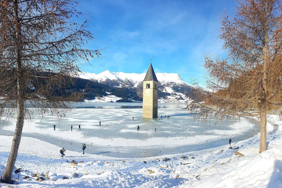 A frozen lake with a tower and mountains in the background.