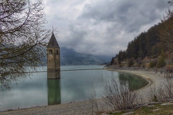 Ein Turm an einem See mit bewaldeter Hügelkulisse im Hintergrund.