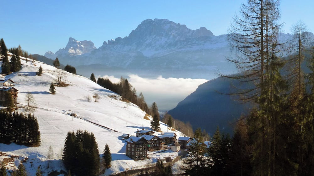 A snow-covered mountain landscape with a chalet, pine trees, and a clear sky.
