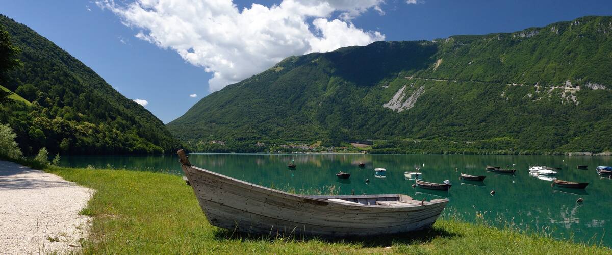 A calm lake surrounded by lush green hills, with several boats anchored in the water and a wooden boat on the shore.