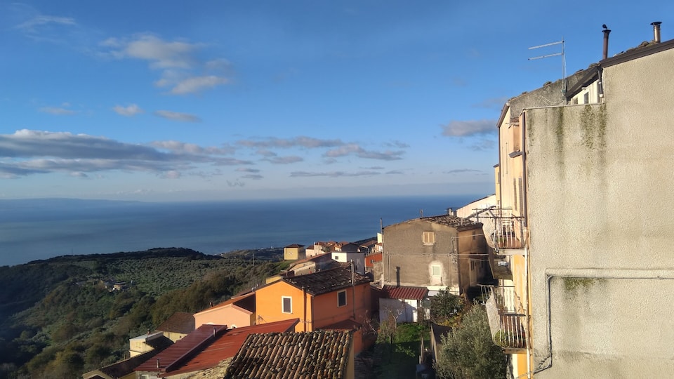 A coastal village with terracotta-roofed houses, a clear sky, and the sea in the background.