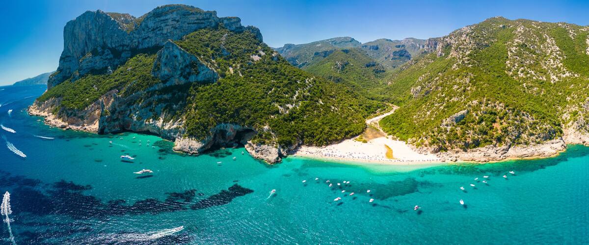 A mountainous island with a beach, clear turquoise waters, and boats.