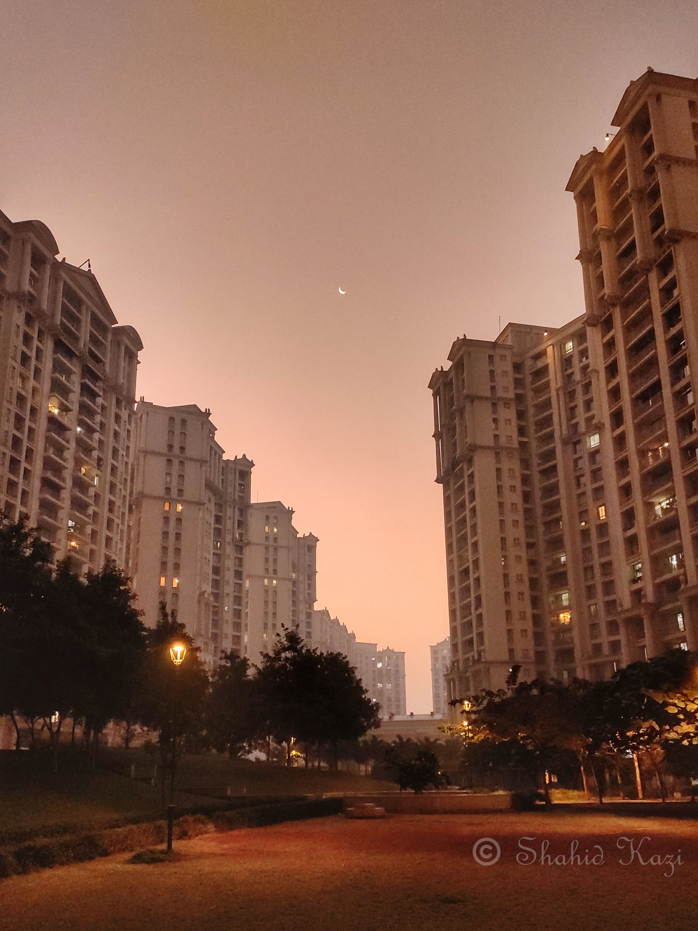 Un atardecer con rascacielos y una luna creciente.