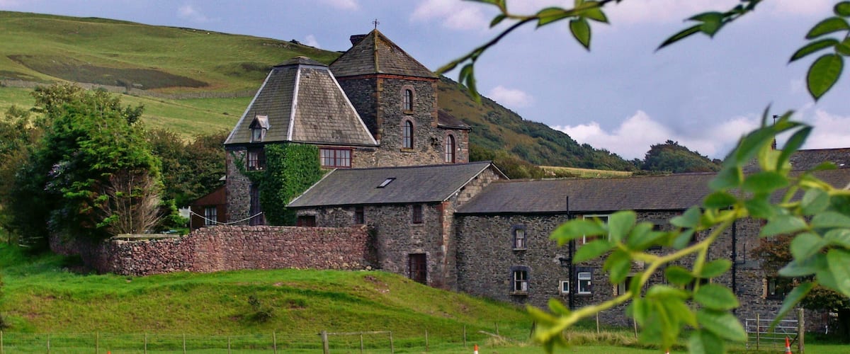 A stone building with a tower, surrounded by green fields and hills.
