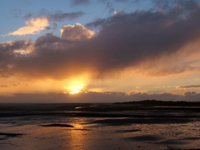 Una puesta de sol sobre una playa con nubes y un mar tranquilo.