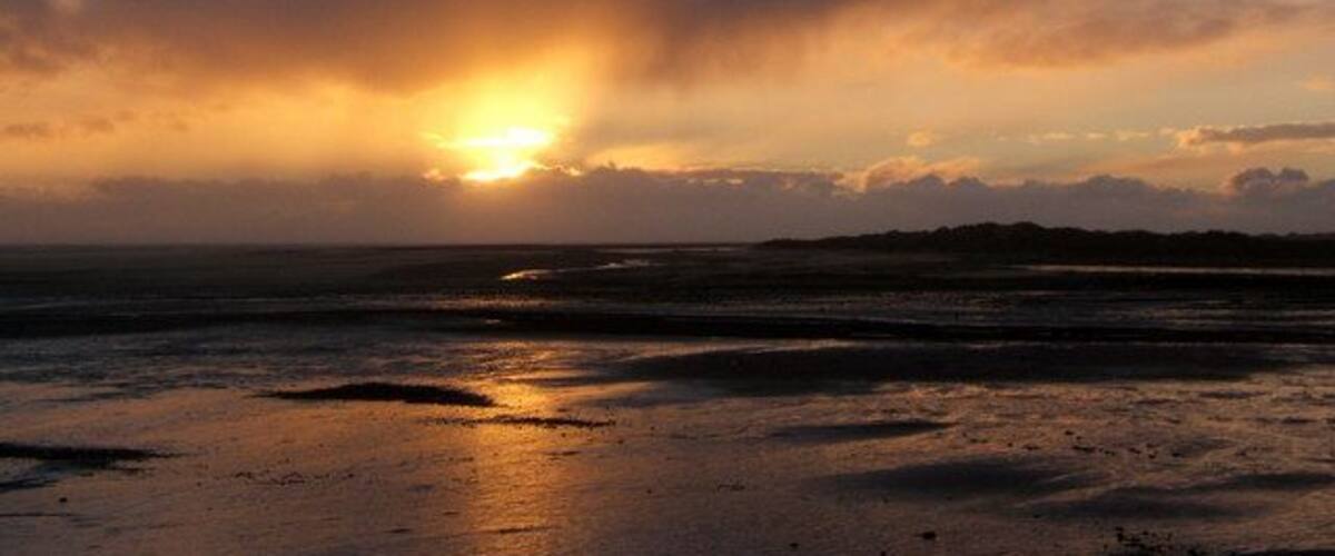 Una puesta de sol sobre una playa con nubes y un mar tranquilo.