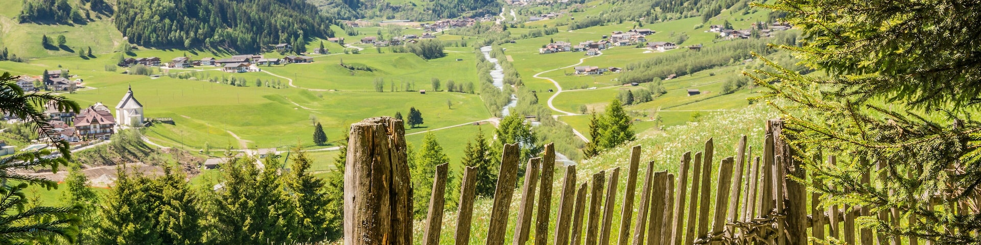 A mountainous landscape with a winding river, green fields, and scattered houses.