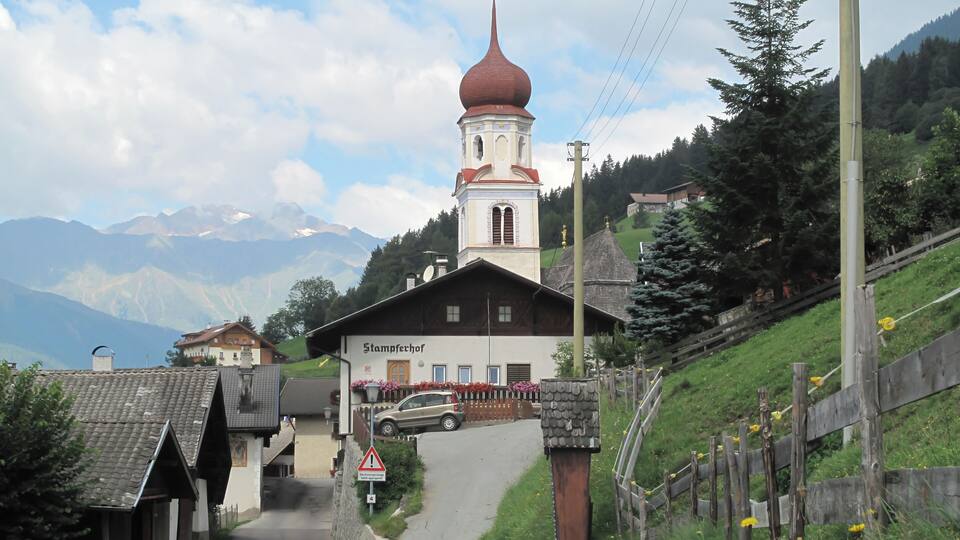 A church with a red dome, a sign reading "Stamperhof," and a winding road leading to it.