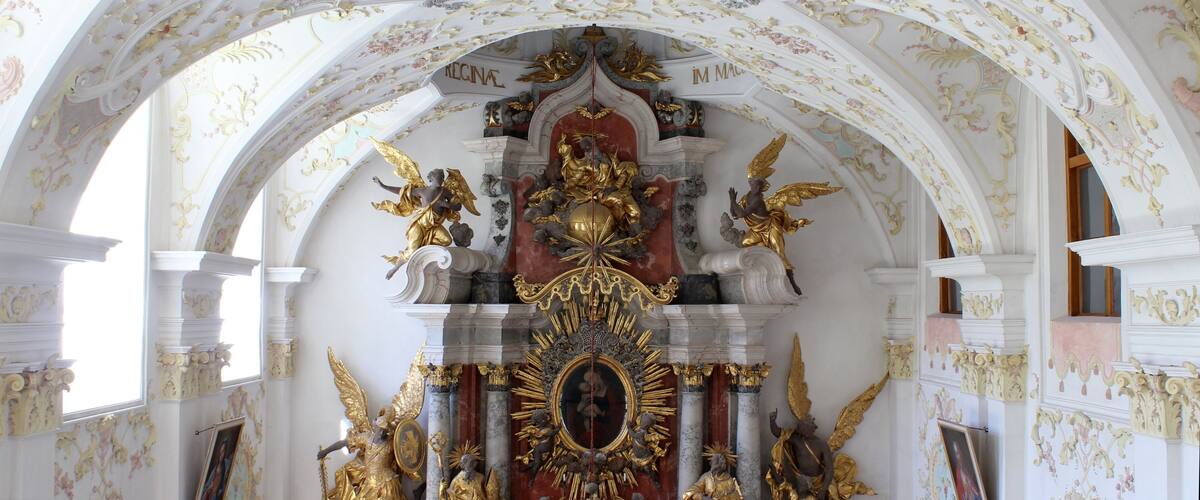 An ornate church interior with a central altar, golden statues, and a ceiling fresco.