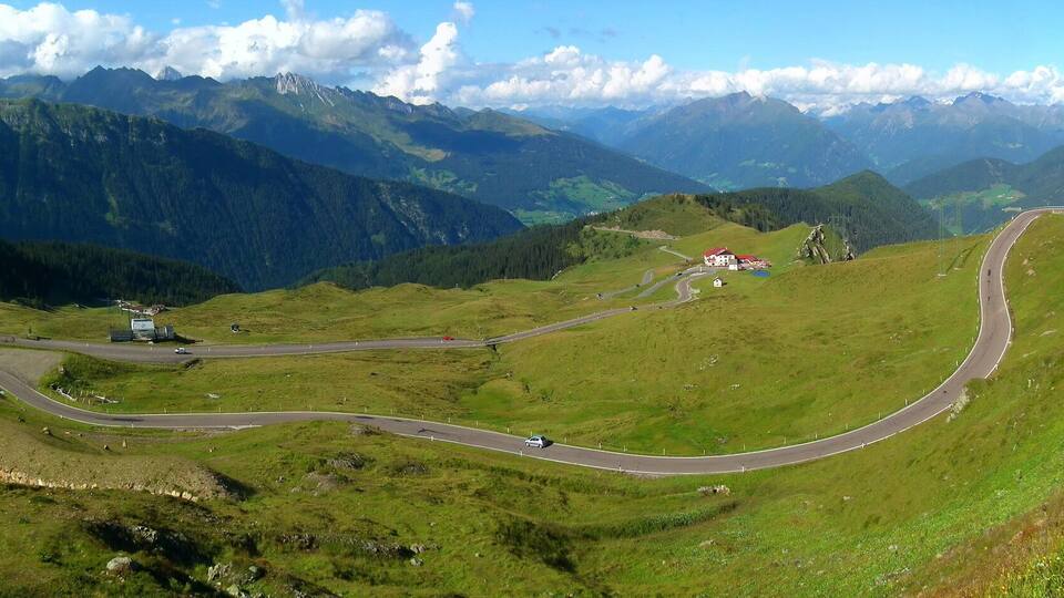 A winding mountain road with a red building and a small house in the valley.