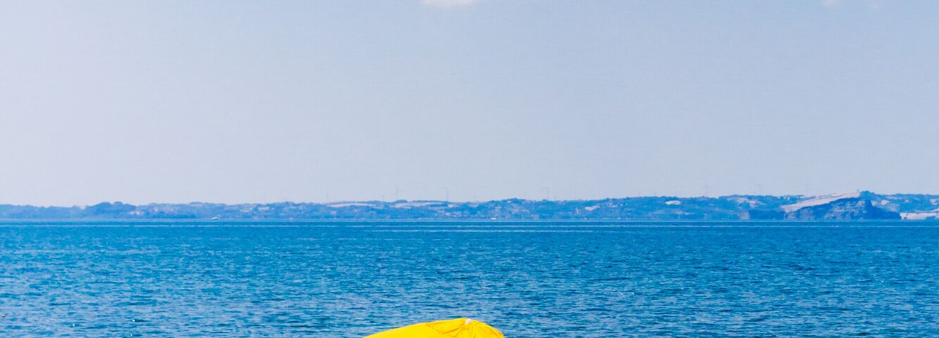 Una playa con una sombrilla amarilla, una bolsa y un enfriador en la arena.