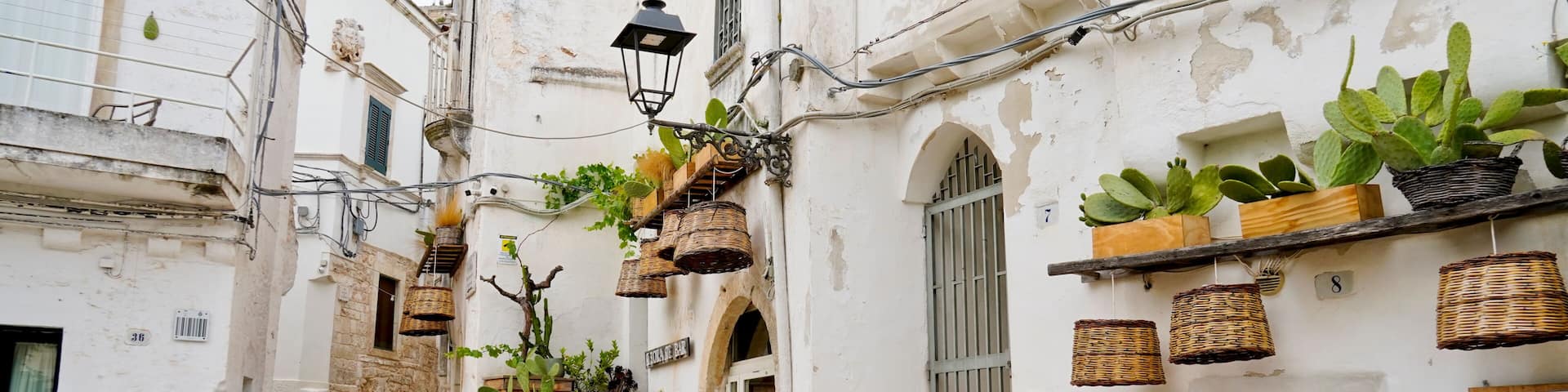 A narrow cobblestone street flanked by white buildings with potted plants and wicker baskets.