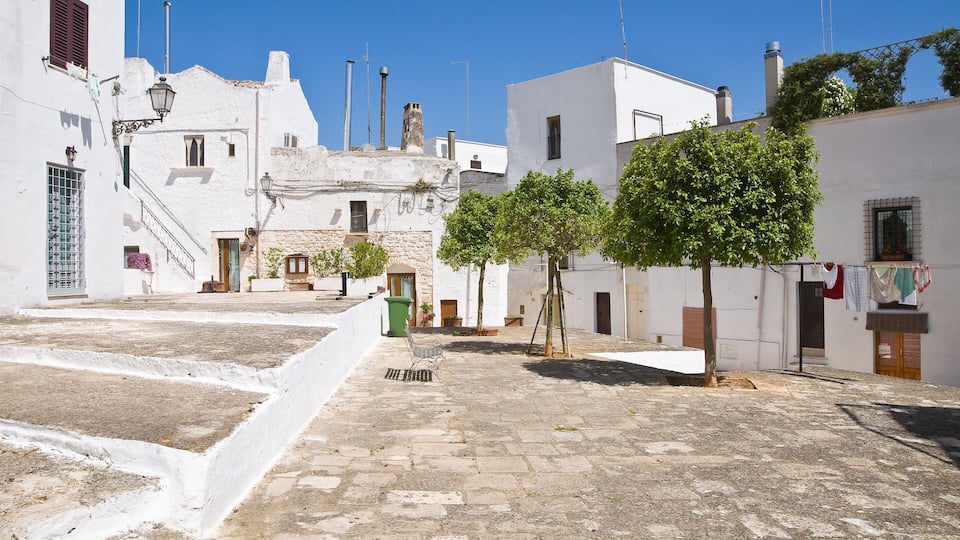 A narrow cobblestone street flanked by white buildings with balconies and laundry hanging out to dry.