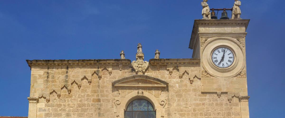 A historic stone building with a clock tower, a large arched window, and a decorative entrance.