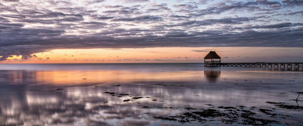 A beach with a thatched-roof hut and a pier extending into the water.