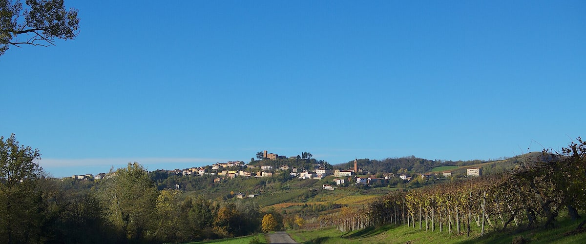 A rural road leading to a hilltop village with scattered houses and a prominent tower.