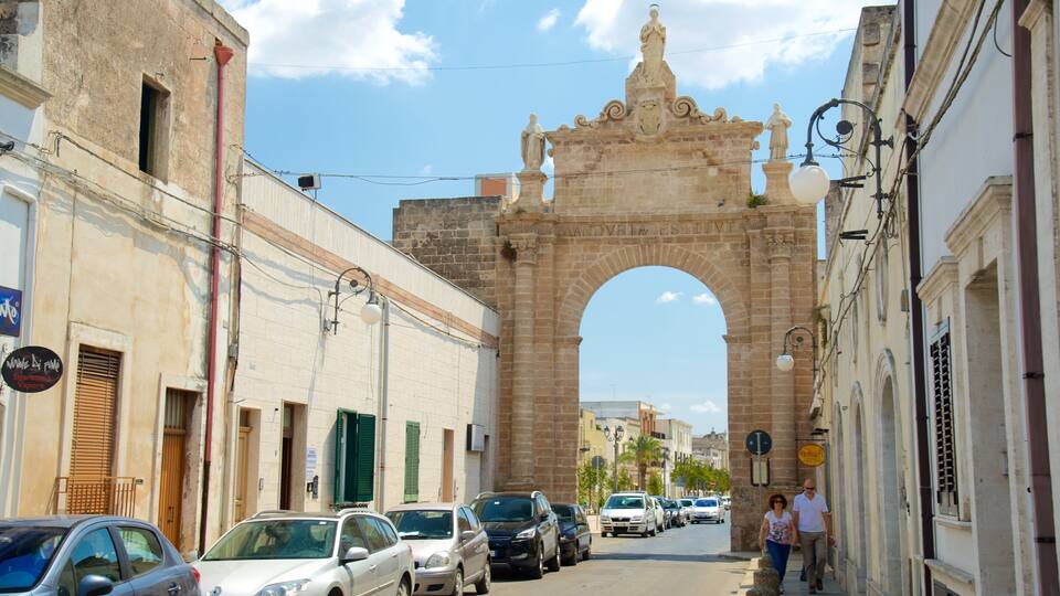 A street with parked cars, a stone archway, and buildings with signs.