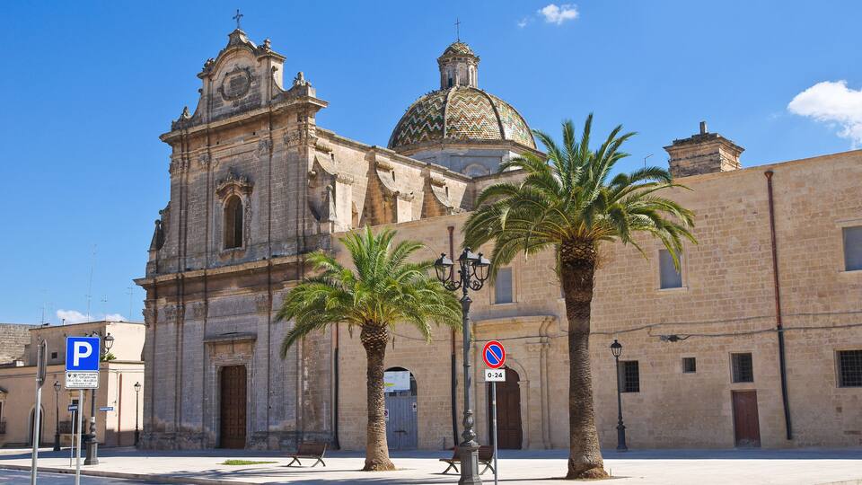 A historic church with a dome and bell tower, palm trees, and a 'No Parking' sign.
