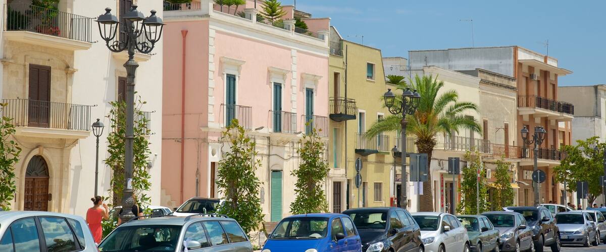 A row of colorful Mediterranean-style buildings with parked cars and palm trees.