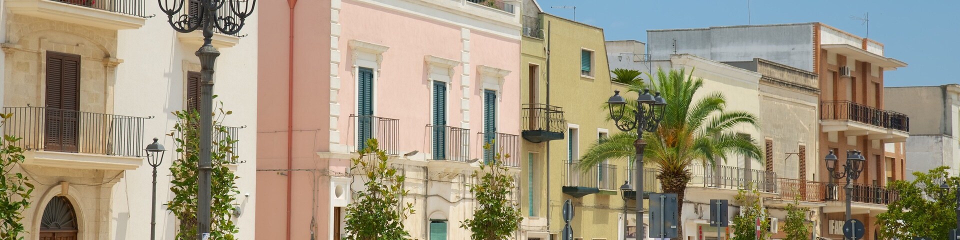 A row of colorful Mediterranean-style buildings with parked cars and palm trees.