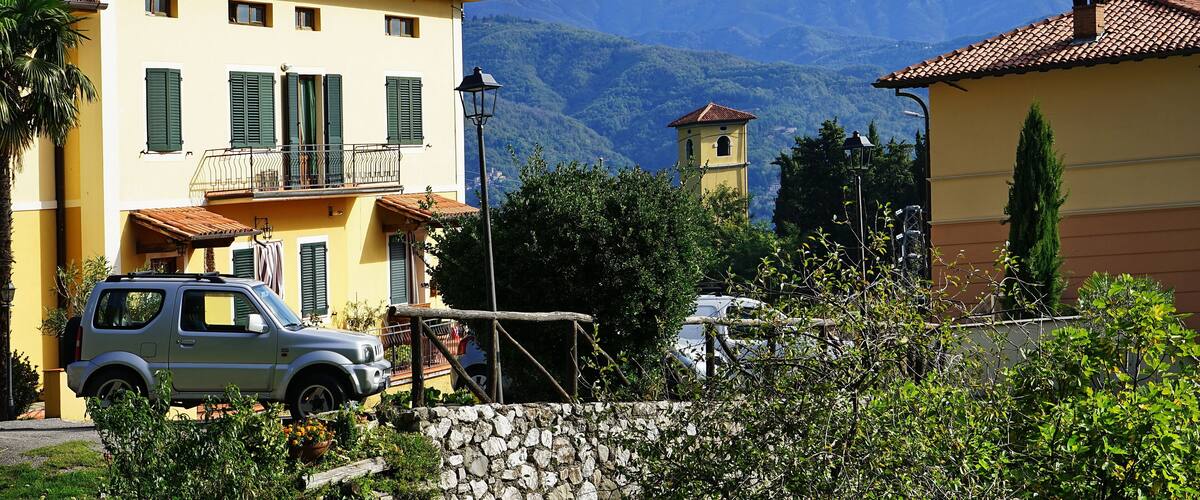 A quaint village with colorful buildings, a parked car, and mountains in the background.