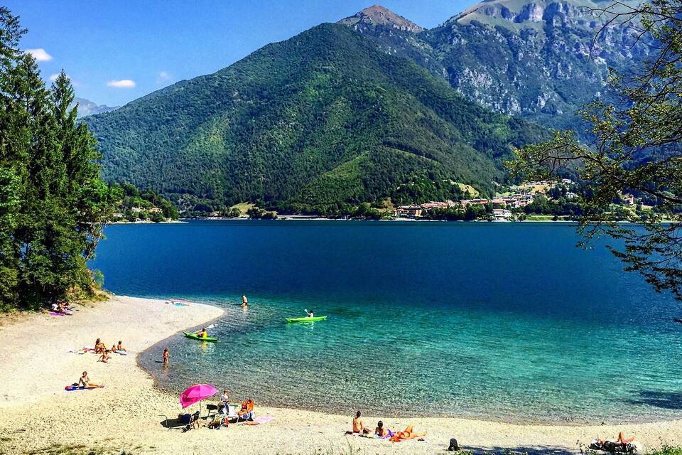 Een strand met helder turquoise water, mensen die zonnebaden, en bergen op de achtergrond.