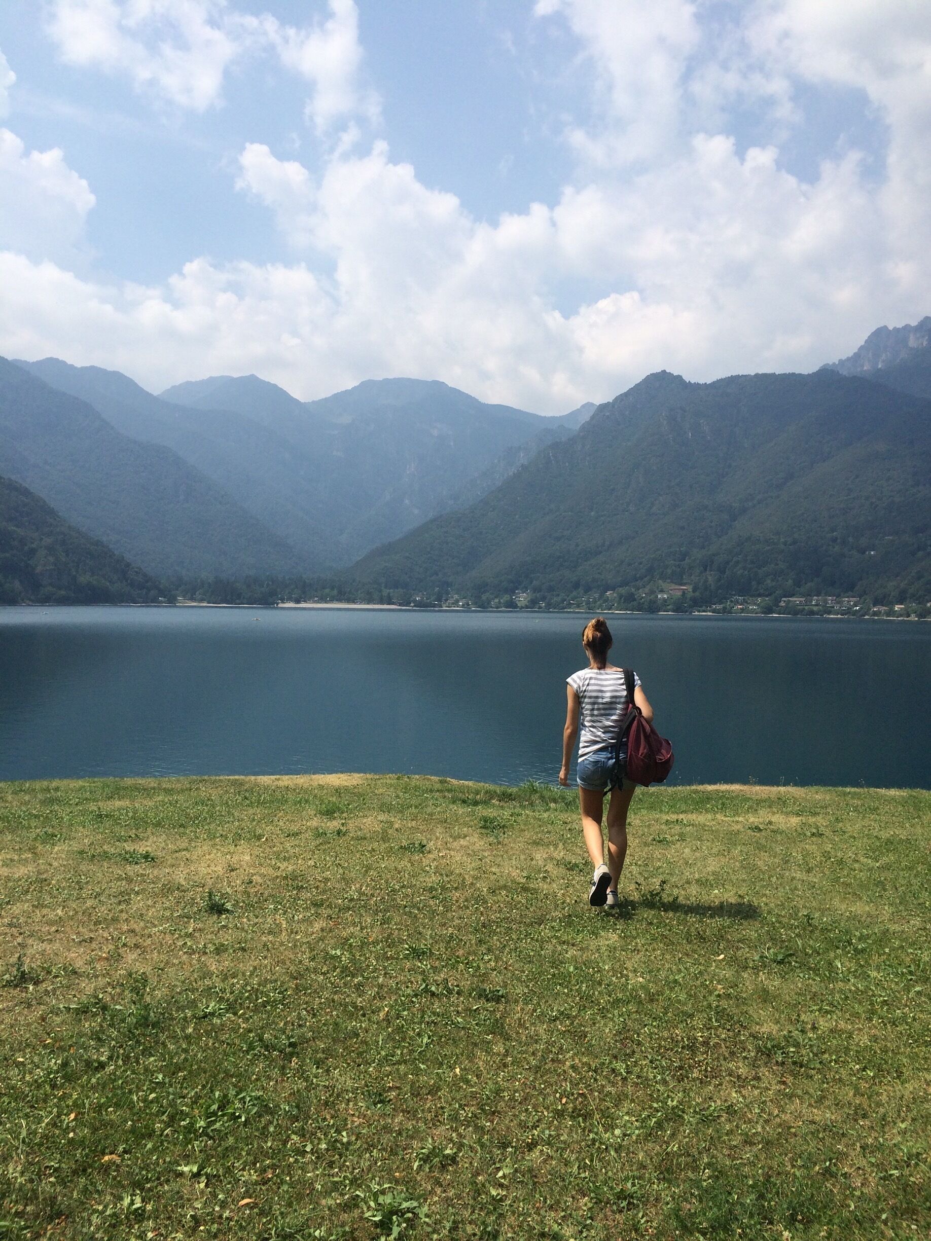 A person walking on a grassy hill overlooking a lake with mountains in the background.
