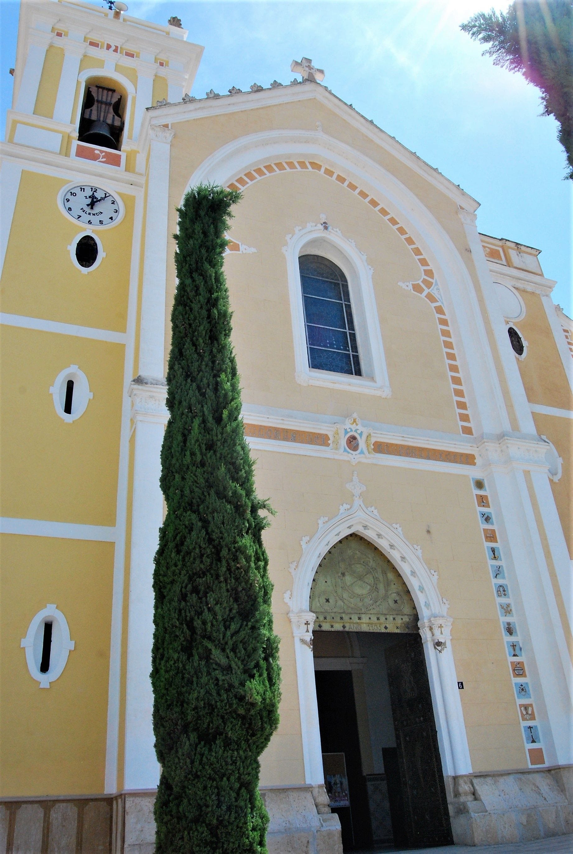 A yellow building with a clock, a tall green tree, and a bell tower.