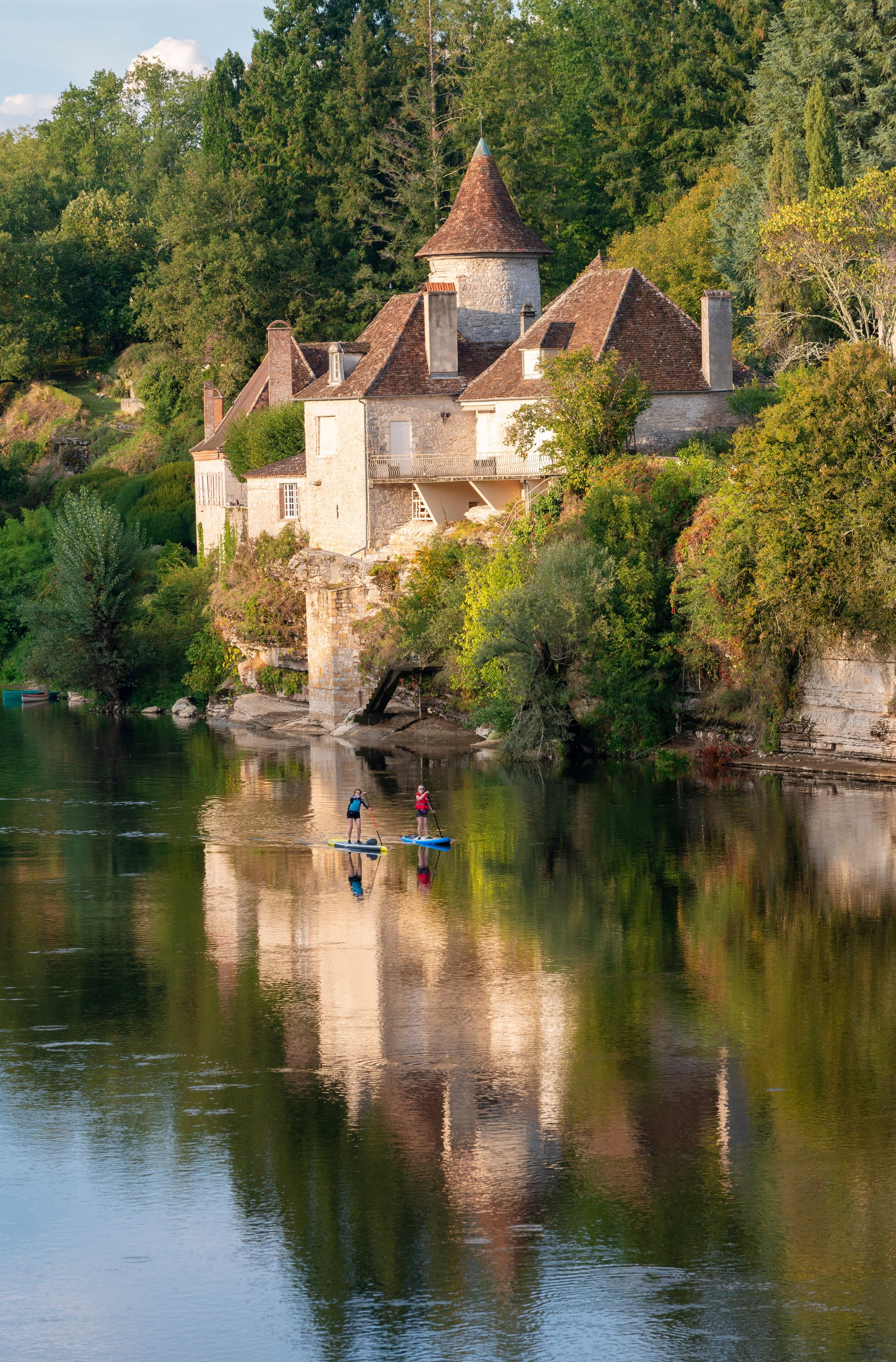 Two women paddleboarding no the River Dordogne in Meyronne, Lot, France, beneath a beautiful chateau