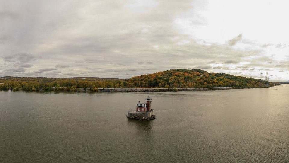 A calm river with a small island covered in autumn foliage and a lighthouse in the center.