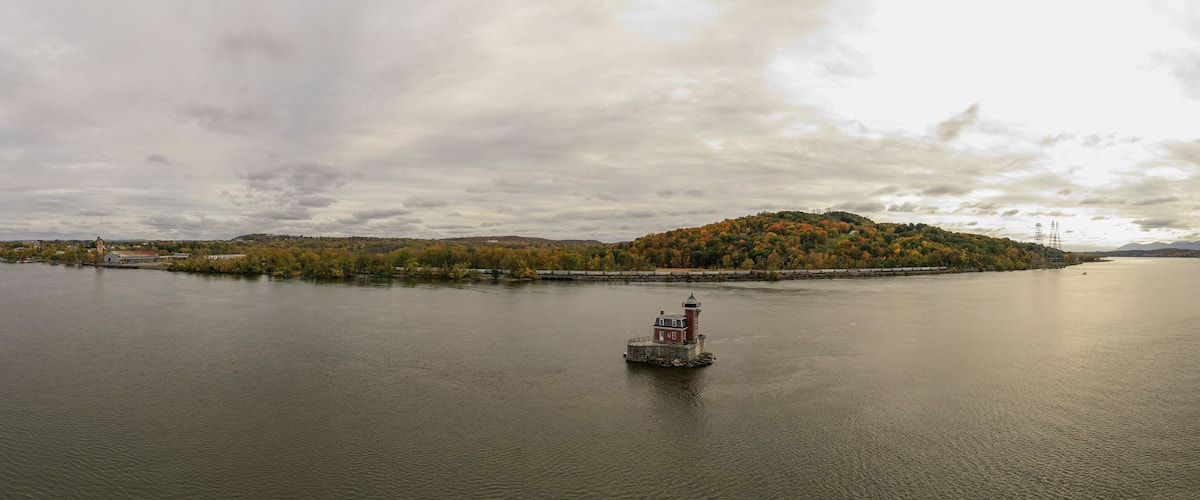 A calm river with a small island covered in autumn foliage and a lighthouse in the center.